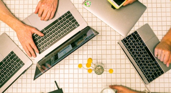 computadores y manos de personas sobre una mesa, vista desde arriba