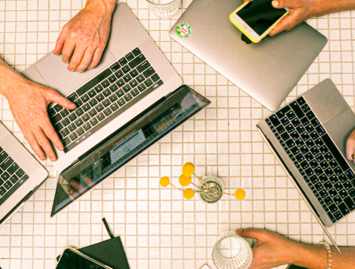 computadores y manos de personas sobre una mesa, vista desde arriba