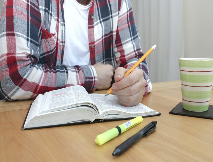 imagen de persona con lápiz sobre libro en escritorio donde hay más útiles y una taza