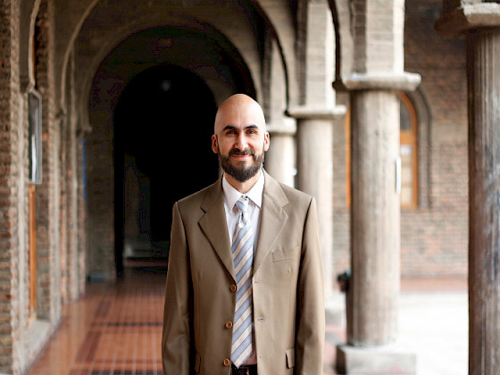hombre, medio plano, mirando de frente, académico Alejandro Vera, en uno de los pasillos del Campus Oriente UC.