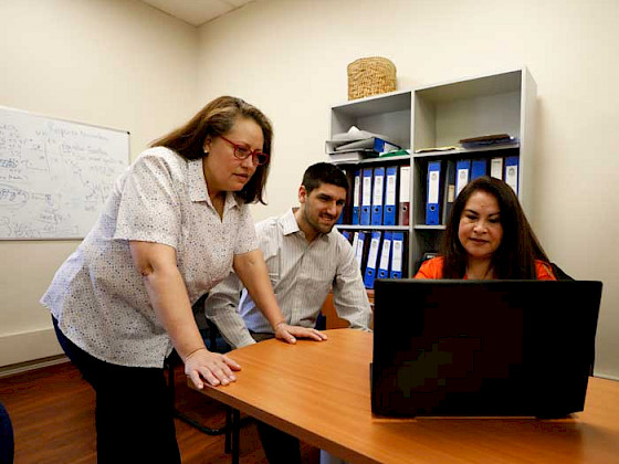 Tres funcionarios de la Vicerrectoría de Comunicaciones (dos mujeres y un hombre) revisan una información en un computador.