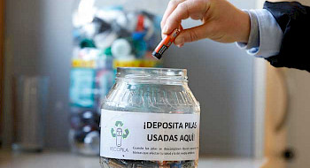 Funcionario deposita una pila en un tacho de reciclaje.