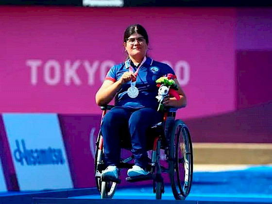 Deportista y estudiante en silla de ruedas mostrando su medalla de plata ante las cámaras.