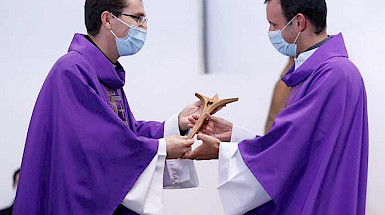 dos sacerdotes, el de la derecha recibe un crucifijo de madera