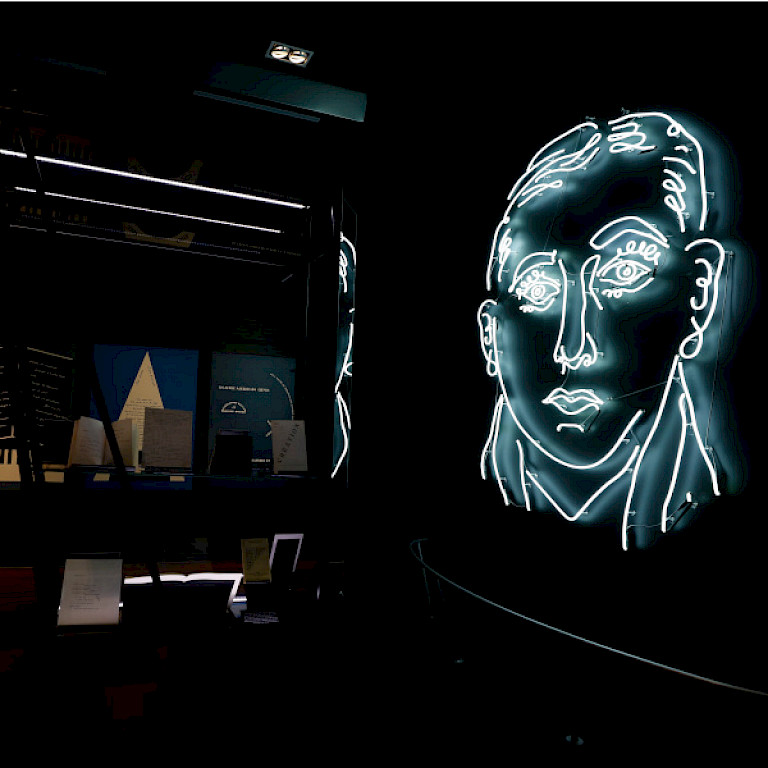 Sala oscura con la imagen del poeta Vicente Huidobro en luces de neón blancas.
