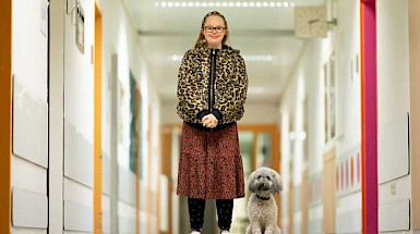 A blond girl with down syndrome is posing for the photo. Next to her is a white poodle dog.