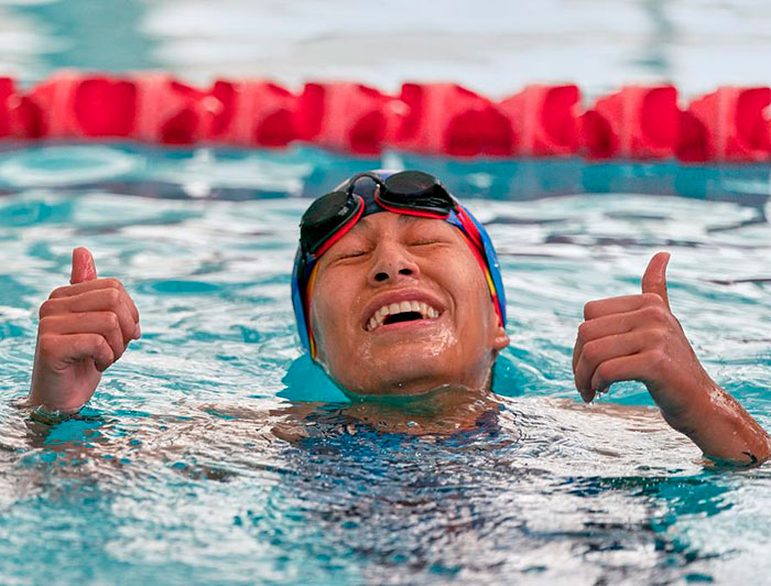 Fotografía de Natalia Gutiérrez en ella piscina, sonriendo y con las manos arriba.
