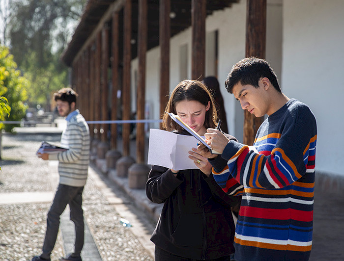Dos jóvenes, hombre y mujer, anotan en sus cuadernos de pie en un patio.