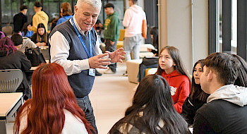 El director del programa Bachillerato Inicia conversando con un grupo de postulantes del programa en una sala; se ven otros jóvenes al fondo.