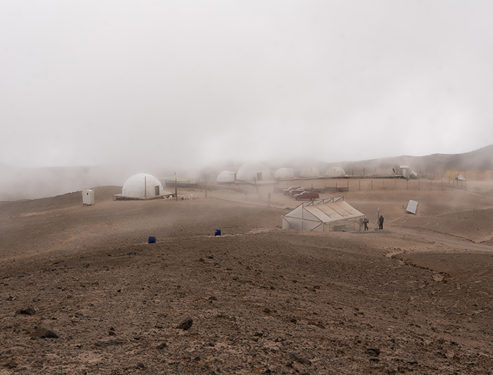 Domes and greenhouse of UC Chile Atacama Station, between hills of earth and covered in fog.