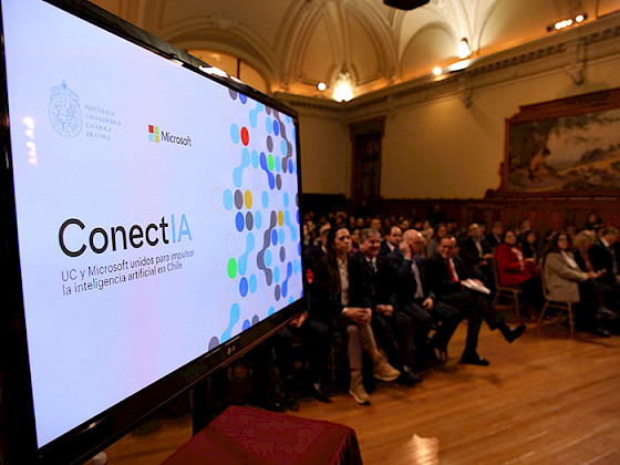 Pantalla donde se ve ConectIA y público de fondo en el Salón de Honor de la UC.