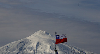 Vista del volcán Villarrica nevado con una bandera chilena al frente.