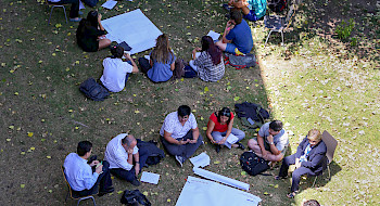 Grupos de personas sentadas en el pasto en círculo.