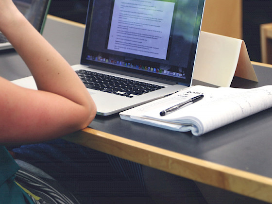 Estudiante mirando un computador con cuaderno al lado.